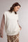 woman wearing a white sleeveless turtleneck sweater over a brown long sleeve top and plaid wide-leg trousers