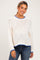 woman wearing a white knit maternity sweater with blue trim and a relaxed fit, smiling at the camera