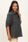 woman wearing a dark green checked maternity shirt with a relaxed fit and short sleeves, smiling while holding the collar