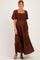 woman wearing a brown smocked maternity maxi dress with puff sleeves and lace detailing, showcasing her baby bump