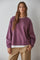 woman wearing a purple oversized sweatshirt with long sleeves and a white shirt underneath, paired with beige pants