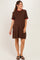 woman wearing a brown maternity dress with a red ruffled collar and sleeves, standing and showing her baby bump