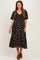 woman wearing a black floral maternity dress with short sleeves and a tiered skirt, smiling and standing with hands on her belly