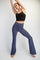 woman wearing a black cropped tank top and navy blue flared yoga pants, striking a pose with arms raised