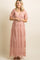 woman wearing a light peach maternity gown with floral embroidery and short flutter sleeves, showcasing her baby bump
