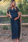 woman wearing a dark blue lace maternity maxi dress and holding her baby bump while standing by a wooden fence