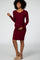 Smiling pregnant woman wearing a long-sleeved burgundy ribbed maternity dress against a grey background