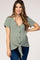 woman wearing a sage green maternity top with short sleeves, button details, and a front tie, showcasing her baby bump