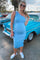 woman wearing a light blue one-shoulder maternity dress with a visible baby bump and white sneakers