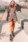 woman in brown short overalls and black combat boots standing on a path with red rock mountains in the background