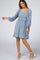 woman wearing a light blue short dress with a square neckline and textured bobble details, posing with one arm lifted