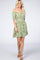 blonde woman wearing a green floral off-the-shoulder mini dress with smocked waist and brown heels