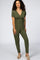 woman with curly hair wearing an olive green short sleeve maternity jumpsuit with a wrap neckline and waist tie