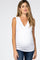 woman wearing a white sleeveless maternity top with a v-neck and a visible baby bump, paired with dark jeans
