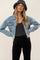 woman wearing a light wash cropped denim jacket with frayed hem and a black bucket hat