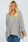 woman wearing a light gray oversized knit sweater with a scoop neckline and long sleeves, paired with blue jeans