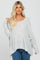 woman wearing a light grey oversized knit sweater with a wide neckline and relaxed fit, paired with blue jeans