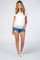 woman wearing a white short sleeve maternity top and distressed denim shorts, showing her baby bump