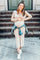 smiling pregnant woman in beige ribbed maternity dress and denim jacket standing on stone steps