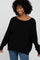 smiling woman with curly hair wearing a black oversized knit sweater and blue jeans