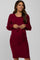 woman wearing a burgundy maternity dress with long sleeves and a tie detail at the waist, showing her baby bump