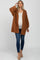 woman wearing a rust-colored oversized maternity cardigan over a white top and blue skinny jeans, showing her baby bump