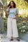 Woman in light blue puff sleeve top and cream wide leg linen pants standing in a garden