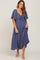 woman wearing a navy blue maxi dress with a tie front and flutter sleeves, standing and smiling