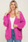 woman wearing a bright pink chunky knit cardigan with pockets over a white top and blue jeans
