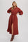 woman wearing a rust-colored long sleeve button-up maxi dress with a tie waist and side slit
