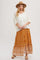 woman wearing a white oversized knit sweater and a flowy rust-colored maxi skirt with floral patterns and embroidery, accessorized with a hat