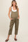 woman wearing a light olive green maternity jumpsuit with buttons and side pockets, showing her baby bump