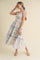 woman wearing a floral print maxi dress with blue and white tones, tied straps, and a flowing skirt