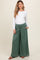 woman wearing a white long sleeve maternity top and green wide leg maternity pants with a baby bump visible