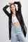woman wearing a black sheer long sleeve button-up shirt over a white crop top and light blue high-waisted jeans