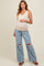 woman wearing a nude maternity tank top and distressed light blue wide-leg jeans, gently cradling her baby bump