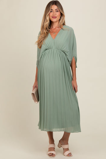 woman wearing a sage green maternity dress with pleats and a v-neck, holding a clutch and showcasing her baby bump