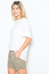 woman wearing a white short sleeve top and olive green shorts, smiling against a white background