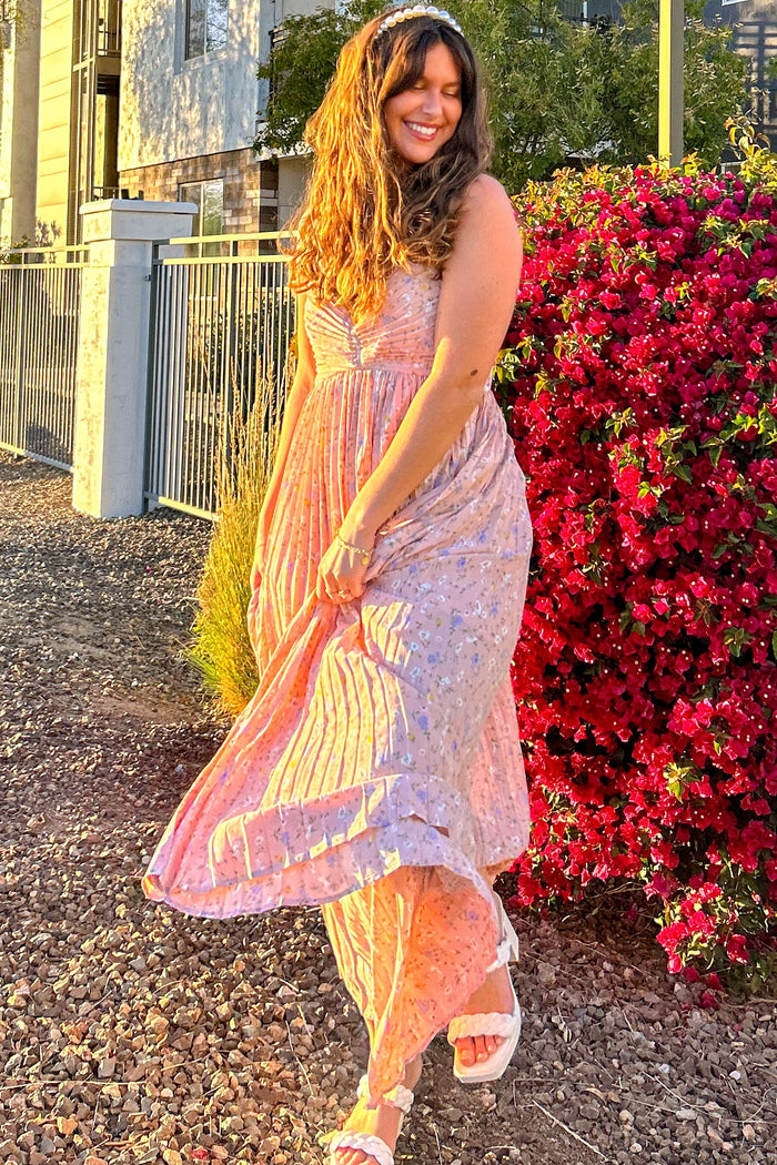 woman wearing a pink floral maxi dress with ruffled edges, twirling in front of blooming flowers
