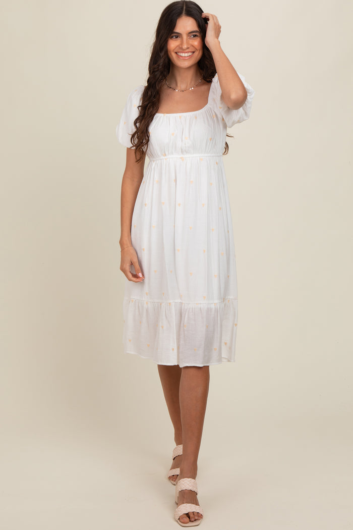 woman wearing a white midi dress with puff sleeves and embroidered details, standing against a neutral backdrop