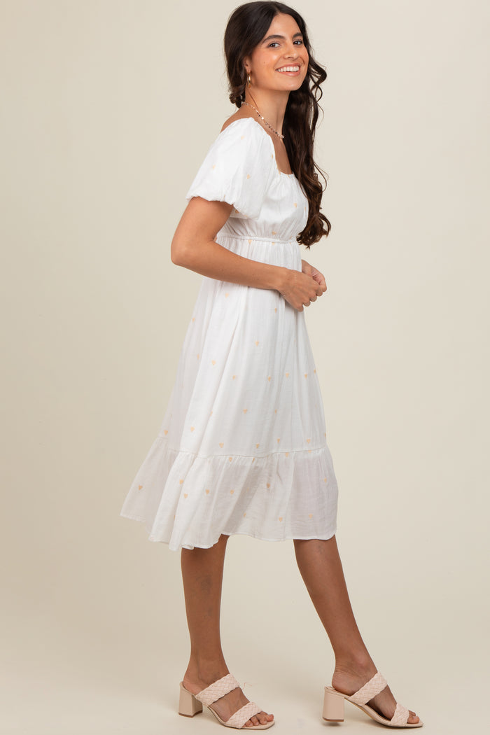 woman wearing a white short sleeve midi dress with embroidered details and ruffled hem, styled with blush sandals