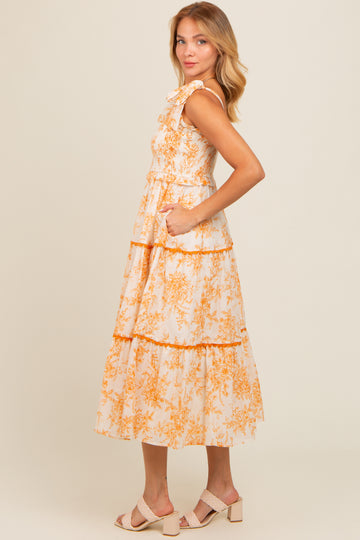 woman wearing a floral print sleeveless midi dress with tiered ruffles and pockets in peach and cream colors