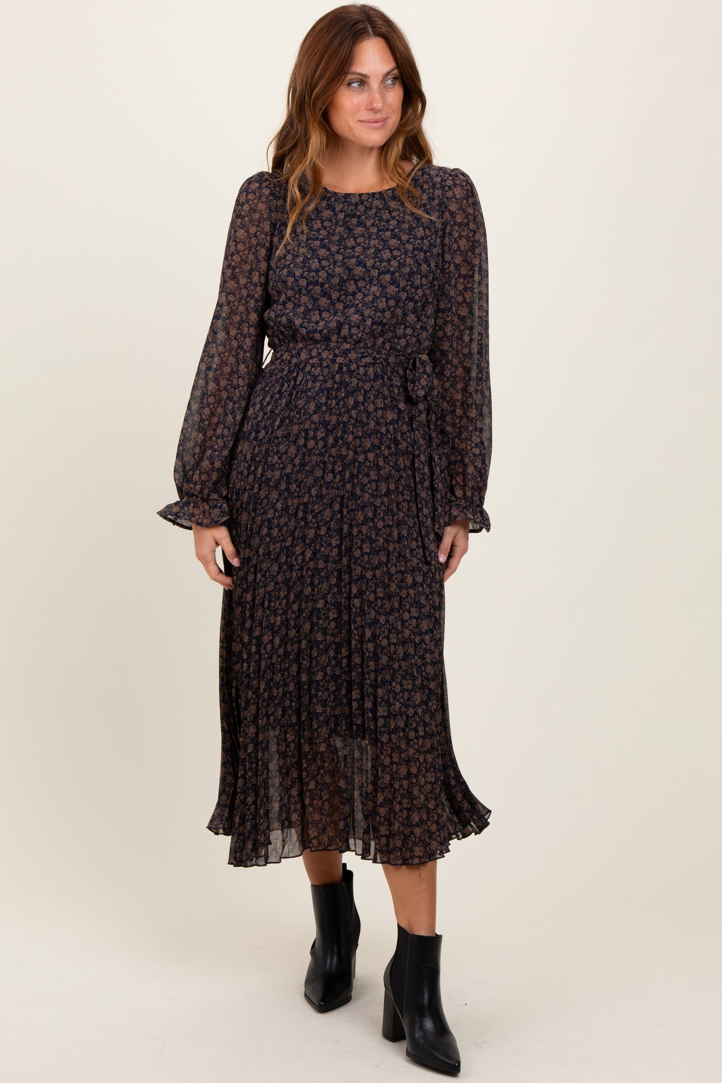 woman wearing a navy floral print midi dress with long sleeves and a tie waist, paired with black ankle boots
