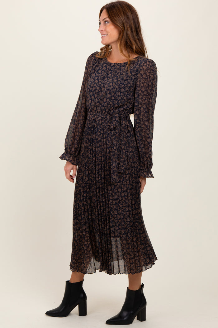 woman wearing a dark floral long sleeve midi dress with a belted waist and pleated skirt, paired with black ankle boots