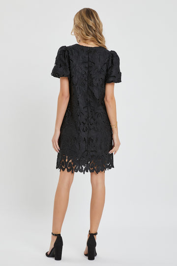 woman wearing a black lace short sleeve dress with a scalloped hem and back zipper detail