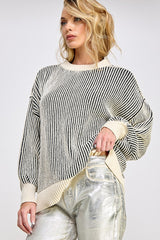woman wearing a black and cream striped oversized sweater with balloon sleeves and side slits, paired with shiny silver pants