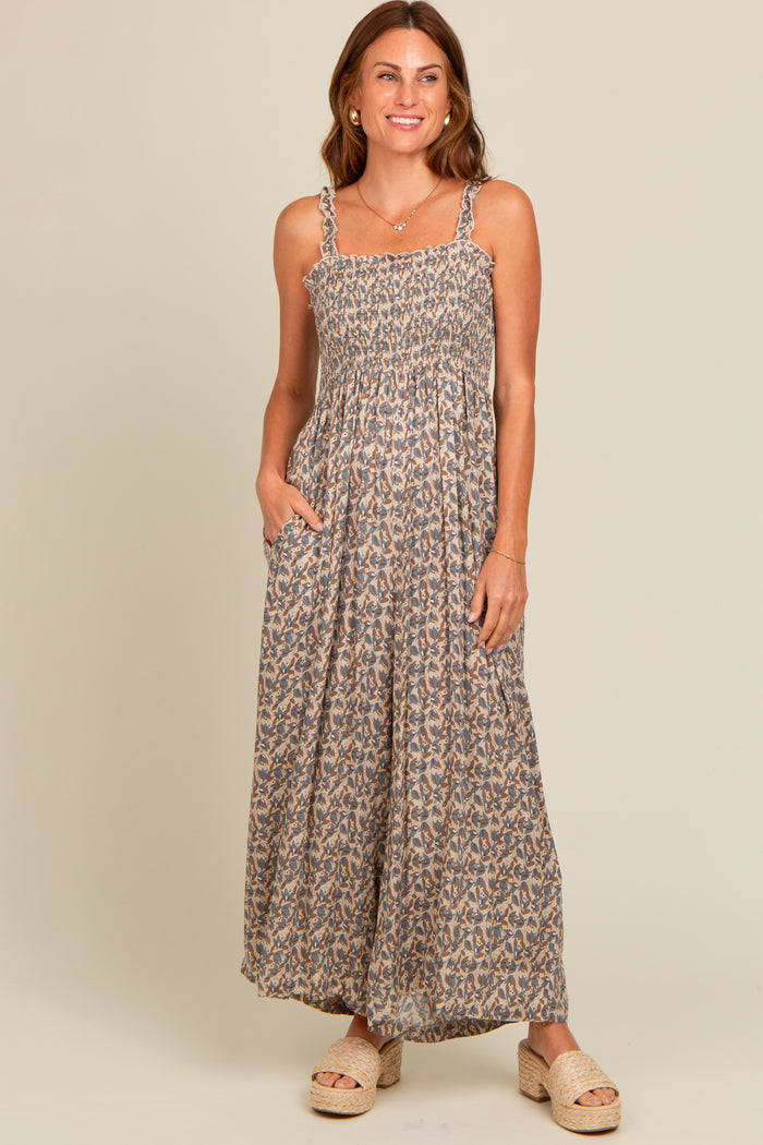 woman wearing a brown floral maxi dress with adjustable straps and pockets, standing and smiling