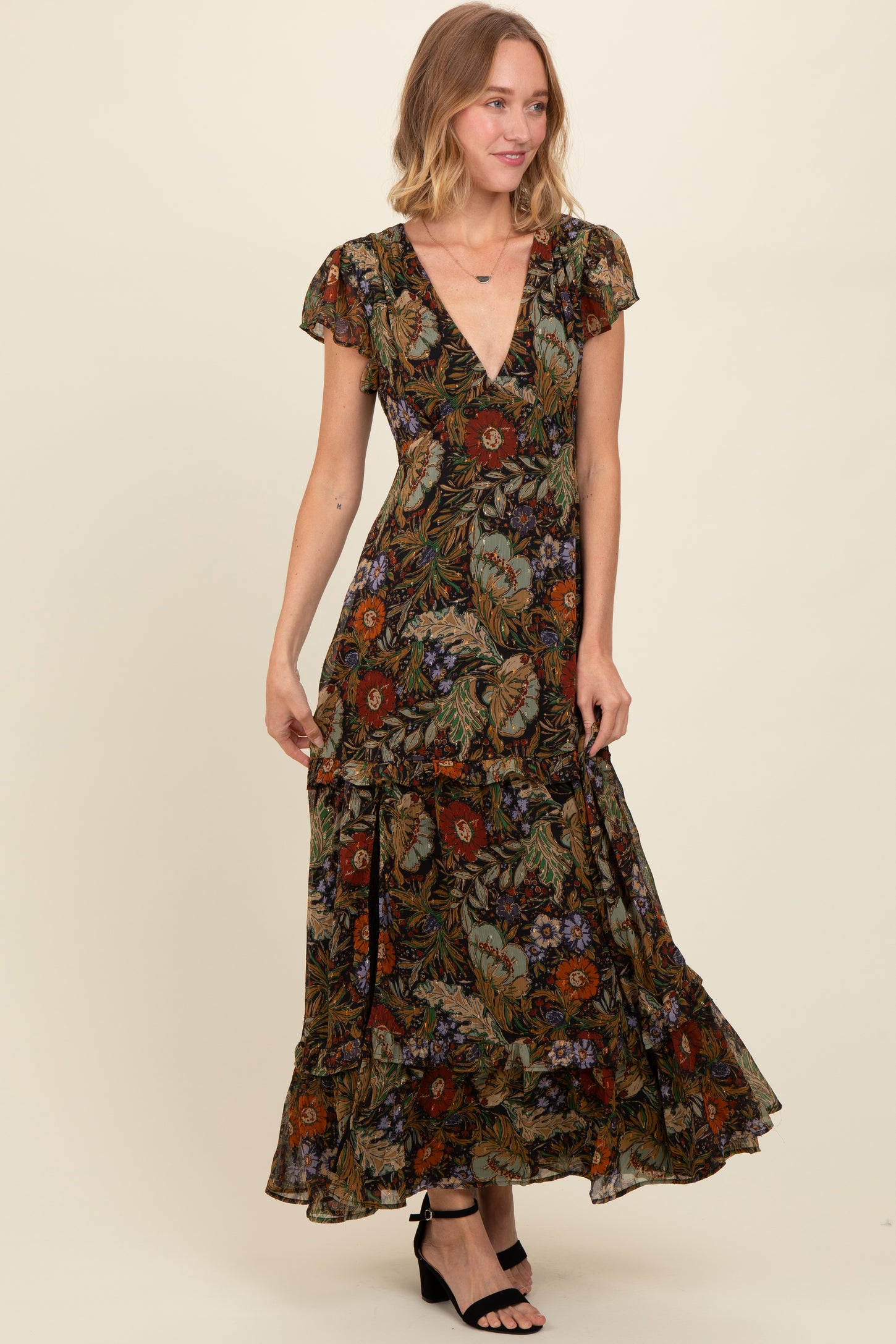 woman wearing a floral print maxi dress with a deep v-neck and ruffled hem, paired with black strappy sandals