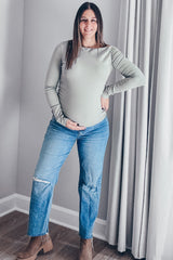 woman wearing a light green long sleeve maternity top and distressed jeans, holding her baby bump