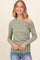 woman wearing a muted green off-shoulder long sleeve top with gathered detail and smiling